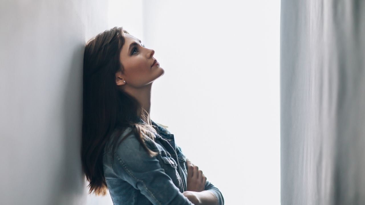 Pessoa olhando pela janela com expressão de tristeza, simbolizando sofrimento no amor.