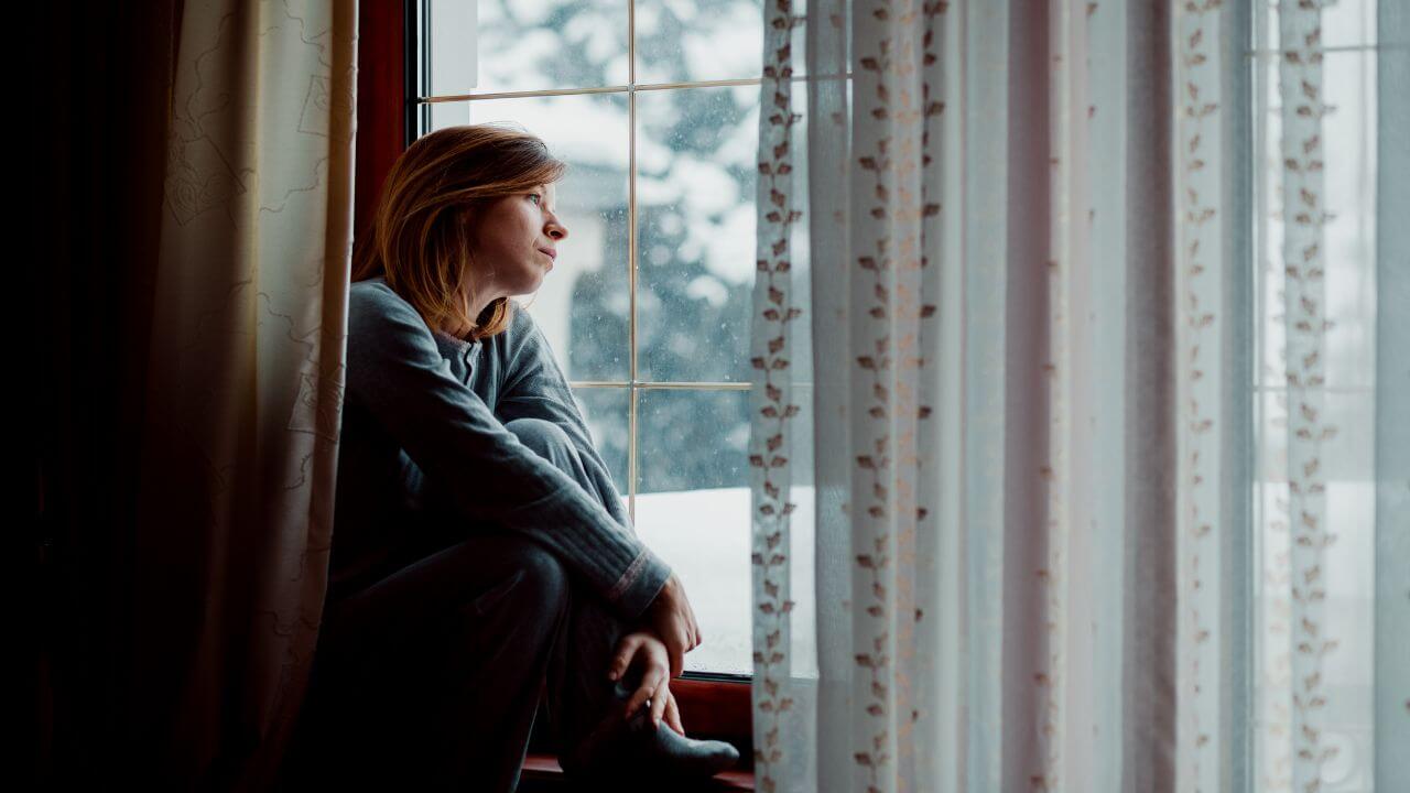 Pessoa olhando pela janela com expressão reflexiva, simbolizando lembranças e cura emocional.